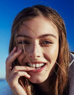 a woman with long hair smiles while holding her hand to her face and looking at the camera