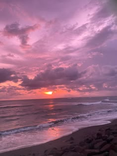 the sun is setting over the ocean with rocks on the beach