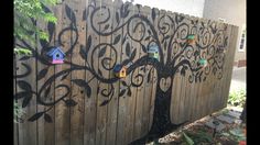 a wooden fence with birdhouses on it and a tree painted on the fence side