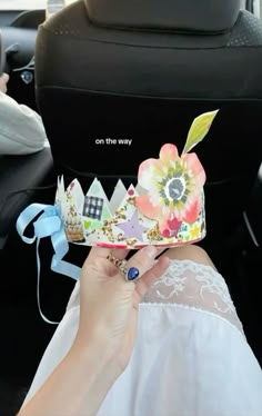 a woman holding up a paper crown in the back seat of a car while wearing a ring