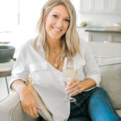 a woman sitting on a couch with a glass of wine in her hand and smiling at the camera