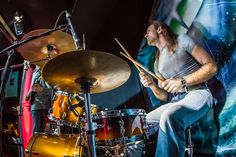 a man sitting on top of a drum set in front of a large poster behind him