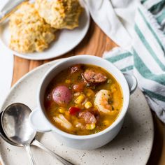 a bowl of soup with shrimp, corn and potatoes on a plate next to a spoon