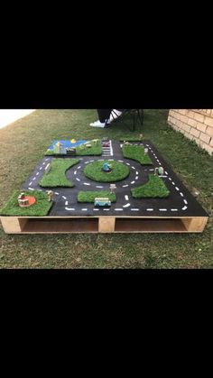 a table made out of wood and artificial grass with cars on the road in the middle