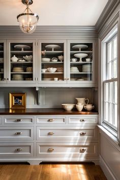 a kitchen with white cabinets and wood flooring next to a light fixture hanging from the ceiling