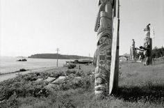 a totem pole sitting on the side of a road next to a body of water