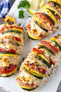 sliced zucchini stuffed with chicken and vegetables on a cutting board next to lemon wedges