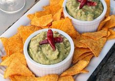 two small white bowls filled with guacamole and chips on a platter