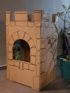 a cardboard castle sitting on the floor next to a potted plant