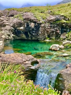 a small stream running through a lush green valley filled with rocks and water surrounded by wildflowers