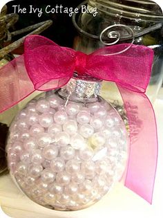 a glass ornament with pink ribbon and white pearls in it on a table