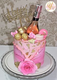 a pink and gold birthday cake on a plate with a bottle of champagne in the middle