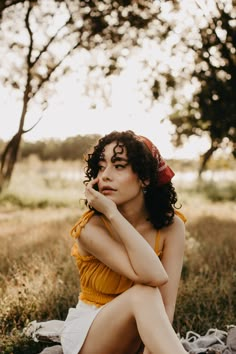 a woman sitting in the grass with her hand under her chin