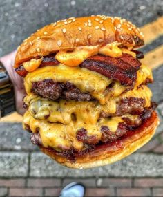 a person holding up a hamburger with cheese and meat