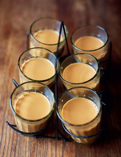 four glasses filled with liquid sitting on top of a wooden table