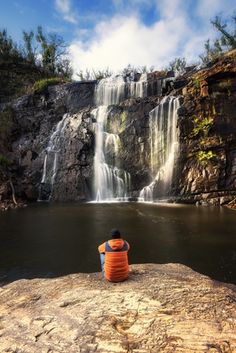 a man sitting on top of a rock next to a waterfall