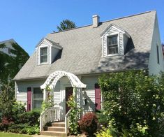 a white house with red shutters on the front and stairs leading up to it