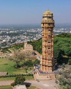 a tall tower sitting in the middle of a lush green field next to a city