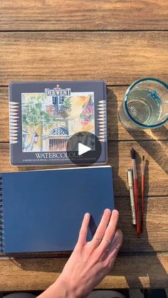 a person's hand on top of a notebook next to some pens and pencils