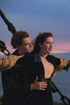 a man and woman standing next to each other on a boat in the ocean at sunset