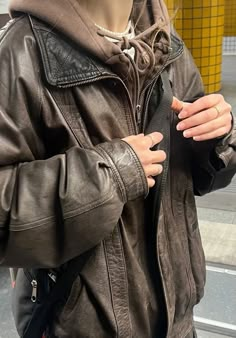 a man in a leather jacket is holding his hand on his hip and looking at his phone