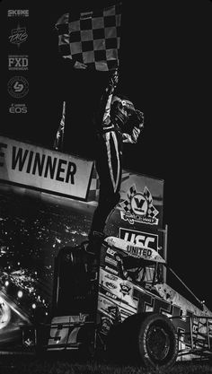 a black and white photo of a man on top of a truck holding a checkered flag