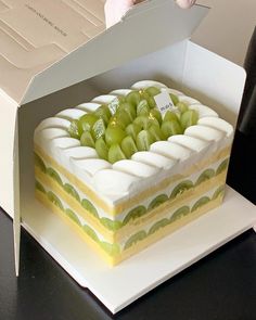 there is a cake in the box with grapes on it and someone holding a knife