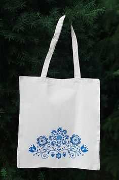 a white tote bag with blue flowers on it hanging from the side of a tree