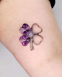 a small purple clover tattoo on the right side of the leg with an amethorate stone embedded in it