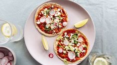 two small pizzas with radishes and cheese are on a plate next to some glasses