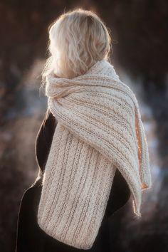 a woman with blonde hair wearing a white knitted scarf and black jacket, back view