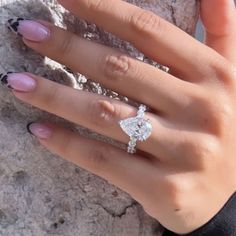 a woman's hand with a ring on top of her finger, next to a rock