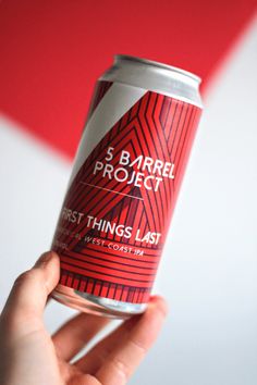 a hand holding a can of beer in front of a red and white background that says 5 barrel project first things last