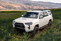 a white toyota 4runner is parked in the middle of a field with mountains in the background