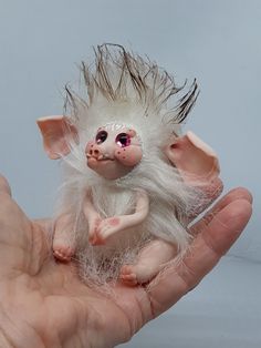 a hand holding a small white troll doll in it's left palm, with pink eyes and long hair