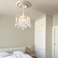 a chandelier hanging from the ceiling in a bedroom with white walls and wood flooring