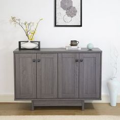 a sideboard with two vases on top of it next to a wall mounted art piece