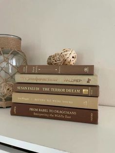 a stack of books sitting on top of a white table next to a vase and lamp