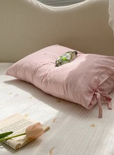 a pink pillow sitting on top of a bed next to an open book and flower