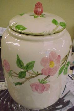 a white vase with pink flowers painted on it and a bird perched on the top