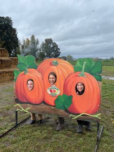 two women standing in front of a sign with three pumpkins on it