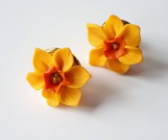 two yellow flower shaped earrings sitting on top of a white table next to each other