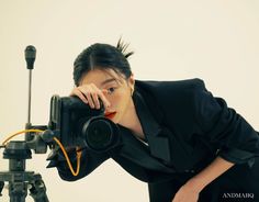 a woman is holding a camera up to her face while leaning on a tripod