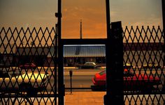 an open gate leading into a parking lot with cars parked on the street behind it