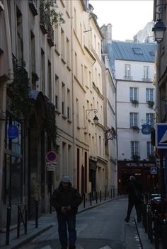 a man walking down the street in an old european city with tall buildings on both sides