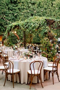 an outdoor dining area with tables and chairs set up for a formal dinner in the garden