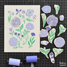 some blue and green flowers are next to two rolls of paper on a cutting board