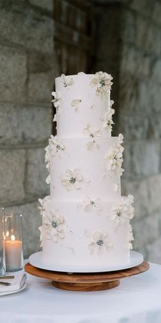 a wedding cake with white flowers on top and candles in the background, sitting on a table