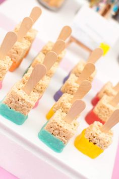 marshmallow pops are arranged on a white plate with wooden spoons sticking out of them