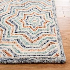 a multicolored area rug on the floor with wooden floors in the background,